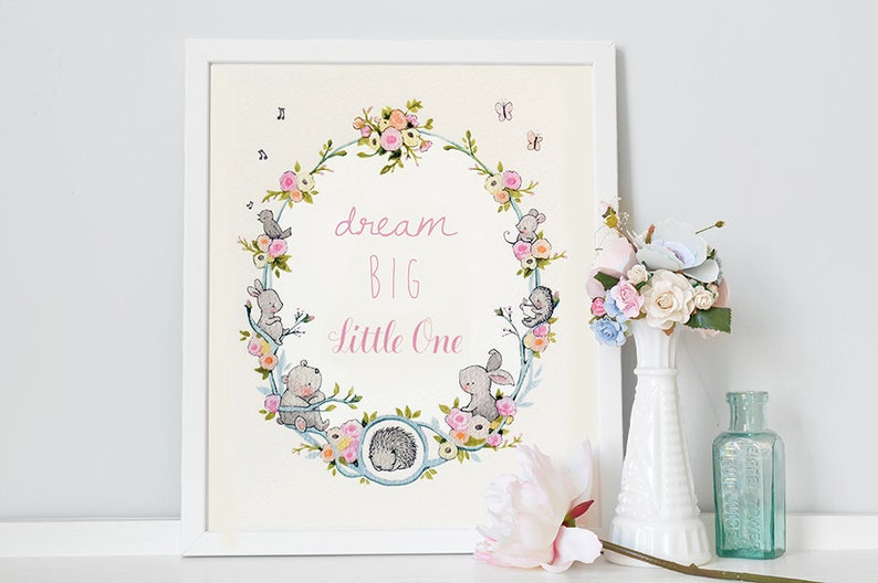 May include: A white framed print with a floral wreath and the text "dream big little one". The wreath is made of flowers, leaves, and small animals. The print is on a white background.