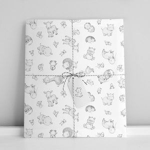 May include: White gift wrap with a black and white pattern of various animals, including a giraffe, a lion, a hippopotamus, and a goat. The gift wrap is tied with a brown string and a white tag with a black and white drawing of a bear.
