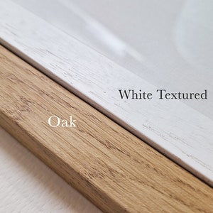 May include: Close-up of a wooden picture frame with a natural oak finish on one side and a white textured finish on the other side. The text "Oak" is printed on the oak side and "White Textured" is printed on the white side.