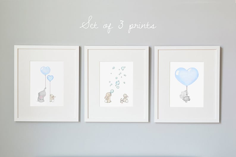 May include: Set of 3 framed prints featuring watercolor illustrations. One print shows an elephant and a smaller animal holding blue heart-shaped balloons. Another depicts bunnies with bubbles. The third shows an elephant holding a heart balloon.