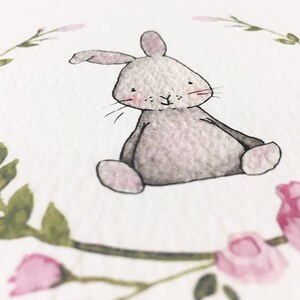 May include: A watercolor painting of a gray bunny sitting in a wreath of pink flowers and green leaves.
