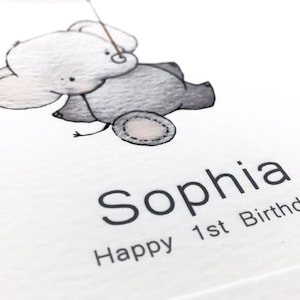 Peut inclure: Une carte blanche avec une illustration noire et grise d'un &eacute;l&eacute;phant tenant une ficelle. Le texte "Sophia Happy 1st Birthday" est imprim&eacute; sous l'&eacute;l&eacute;phant.