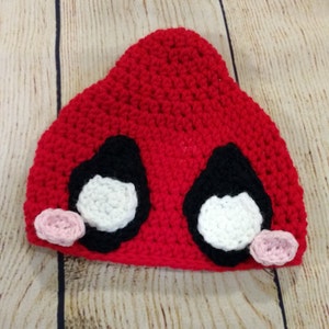May include: Red crocheted hat with black and white eyes and pink ears.