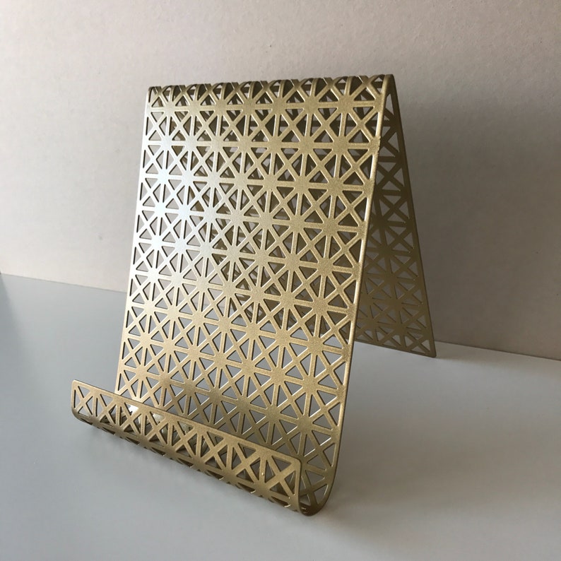 May include: A gold metal phone or tablet stand with a geometric pattern. The stand is made of thin metal and has a curved base.