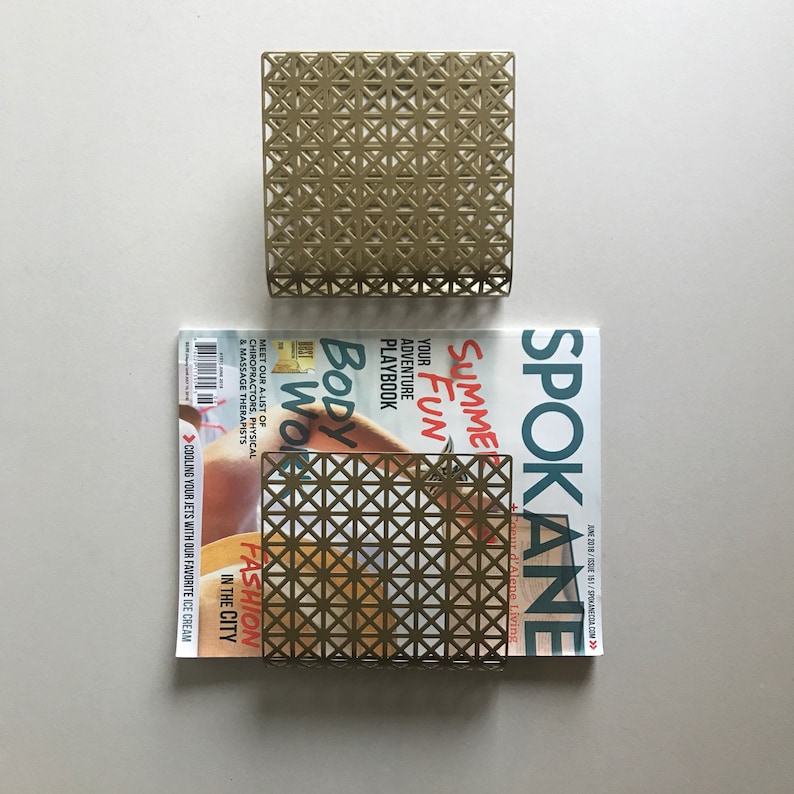 May include: Gold metal magazine holder with a geometric pattern. The holder is sitting on top of a magazine with the text "Spokane" and "Summer Fun" on the cover.