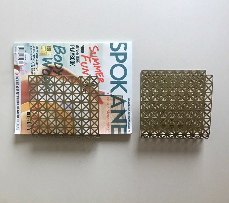 May include: A gold metal magazine rack with a geometric pattern. The rack is holding a magazine with the title "Spokane Summer Fun" on the cover.