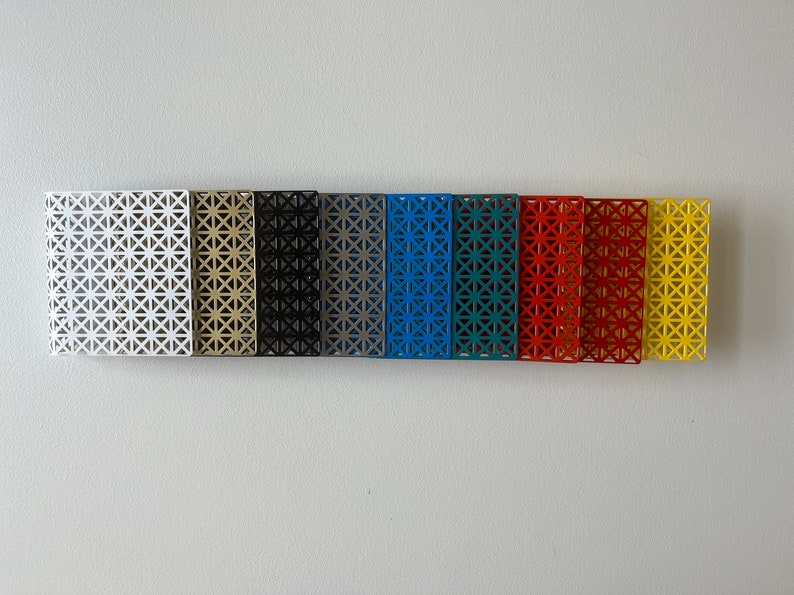 May include: A row of ten metal squares with a geometric pattern, each painted a different color: white, gold, black, gray, blue, teal, red, orange, yellow, and white.