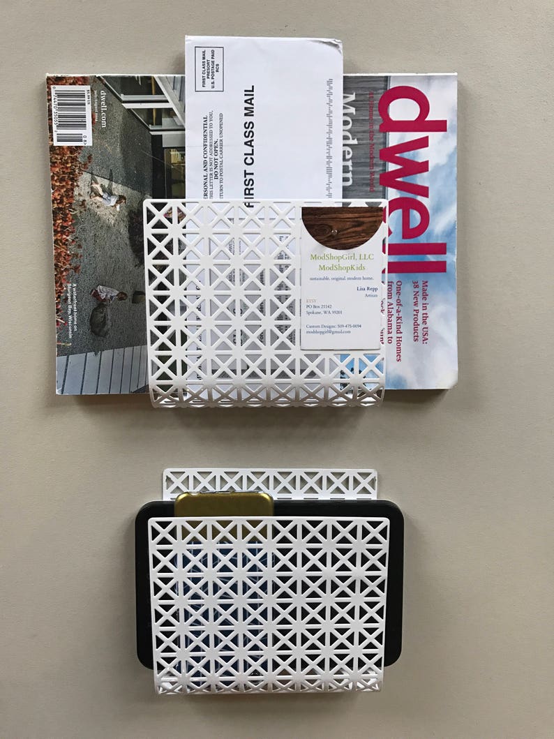May include: Two white metal wall organizers with a geometric pattern. The top organizer holds a magazine and a business card. The bottom organizer holds a black tablet.