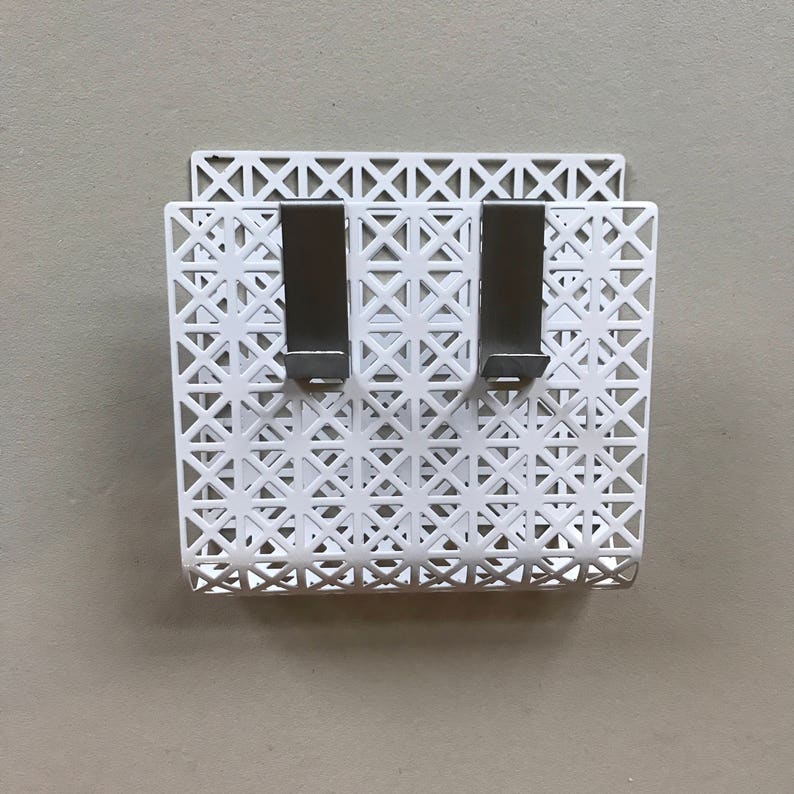 May include: White metal wall organizer with a geometric pattern and two hooks.