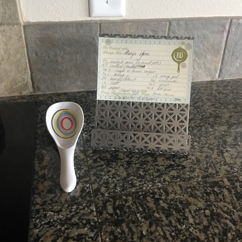 May include: A handwritten recipe card for Mary's Yams, with ingredients and instructions, displayed in a metal stand on a countertop. The recipe calls for sweet potatoes, brown sugar, orange juice, ginger, salt, and pepper. The card is labeled "PD" in the top right corner.