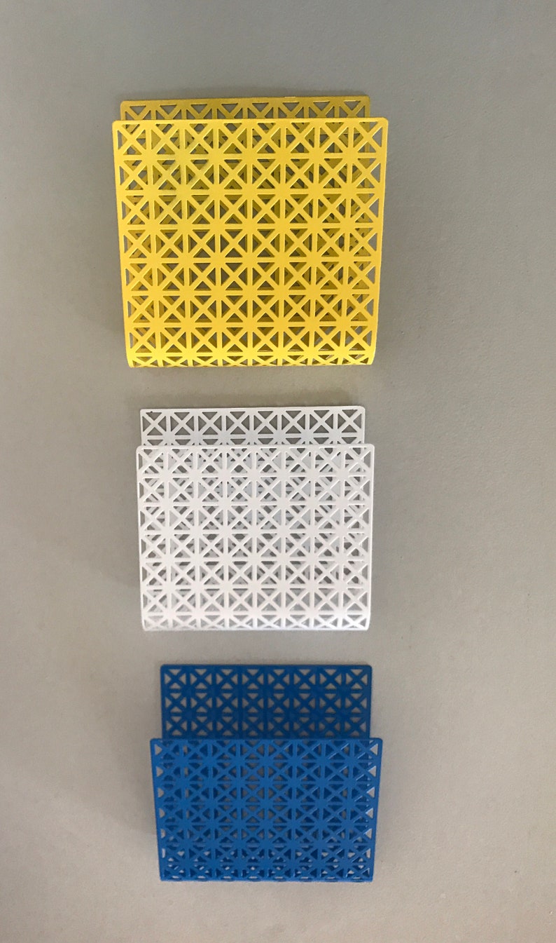 May include: Three metal napkin holders with a geometric pattern. The holders are yellow, white, and blue.