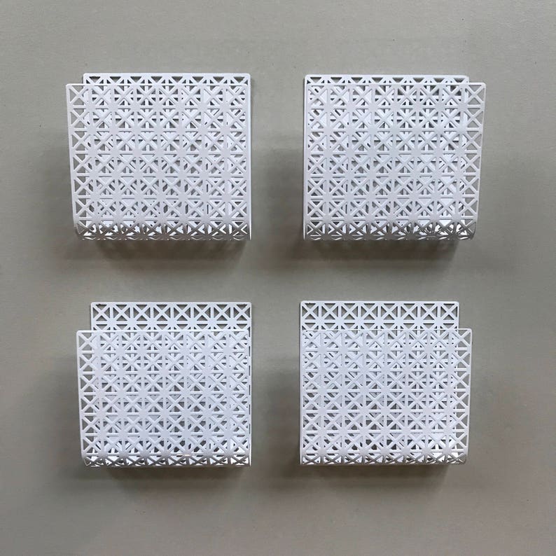 May include: Four white metal wall mounted magazine holders with a geometric pattern.
