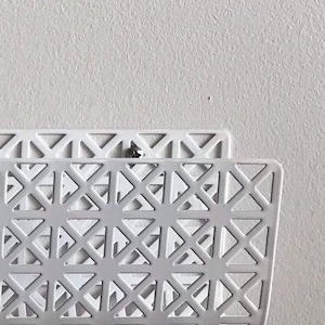 May include: White metal magazine rack with a geometric pattern. The rack is mounted to a white wall.