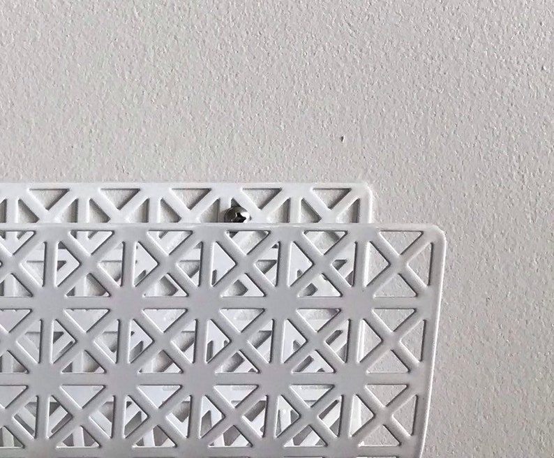 May include: White metal magazine rack with a geometric pattern. The rack is mounted to a white wall.