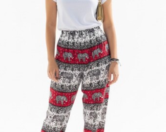 May include: A woman wearing a white t-shirt and patterned pants. The pants feature a red and white design with elephant motifs. The pants are paired with white high heels and a small gold purse.