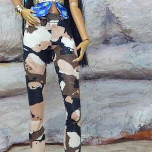 May include: A fashion doll in a blue patterned halter top with a gold waist detail, and camouflage leggings. The doll is accessorized with gold bracelets and gold pointed-toe heels. Long black hair completes the look.