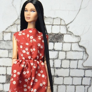 May include: A doll wearing a red sleeveless dress with white floral print, black tights, and black boots with silver buckles.