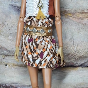 May include: A fashion doll with dark curly hair wearing a brown sleeveless top with a white textured front panel, a patterned skirt with brown, white, and orange geometric shapes, a gold metallic belt, a long pendant necklace, and beige boots.