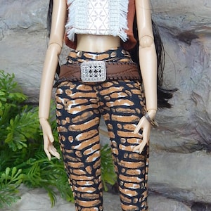 May include: A fashion doll with long dark hair wearing a rust-coloured sleeveless crop top with a white fringed centre panel, paired with black and brown patterned trousers and a brown belt featuring a silver rectangular buckle and tan heels.