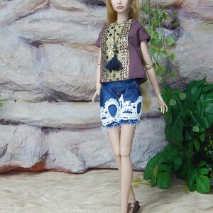 May include: A fashion doll with long blonde hair wearing a brown short-sleeved top with a gold sequined front panel and a dark blue denim skirt featuring a white lace trim at the hem. The doll is wearing metallic bronze slip-on shoes.
