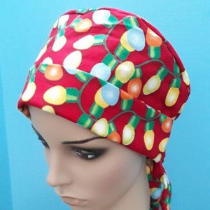May include: Red fabric head covering with a pattern of colorful Christmas lights. The head covering is tied at the back of the neck with a long tail.