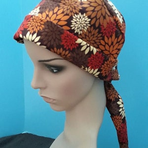 May include: A brown, red, and cream floral print head covering with a long tie. The head covering is tied at the back of the neck and the tie hangs down the back.