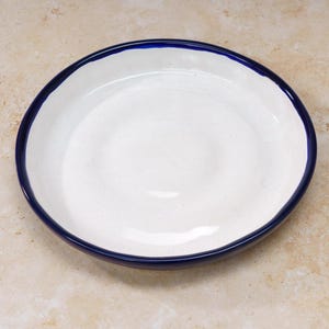 May include: A white ceramic serving dish with a dark blue rim. The dish is round and shallow.