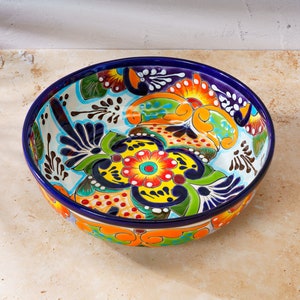 May include: A large, colorful ceramic bowl with a blue rim and a floral design. The bowl is decorated with bright colors, including yellow, orange, red, green, and blue.