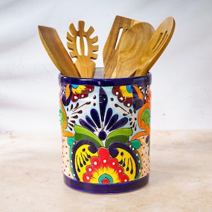 May include: A colorful ceramic utensil holder with a vibrant floral design in red, yellow, blue, and green. It contains several wooden kitchen utensils, including spatulas and slotted spoons. The holder is approximately 6 inches tall.