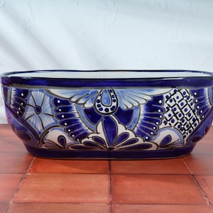 May include: A large, oval-shaped ceramic planter with a blue and white floral design. The planter has a dark blue rim and a white background with intricate blue floral patterns.