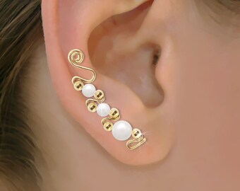 May include: Gold ear cuff with white pearls and a delicate wire design. The cuff is worn on the upper part of the ear.