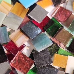 May include: A variety of small, square glass tiles in various colors, including red, green, blue, brown, and black. The tiles are arranged in a random pattern and are perfect for crafting projects.