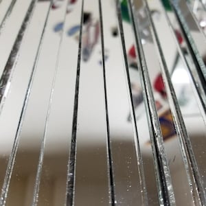 May include: A close-up of a stack of narrow, rectangular mirror tiles. The tiles are arranged vertically, creating a reflective surface with a slight distortion.