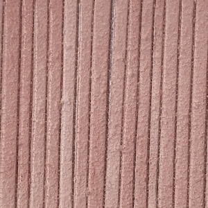 May include: Close-up of a textured, reddish-brown surface with vertical lines. The lines are evenly spaced and create a ribbed effect. The material appears to be leather or a similar material.