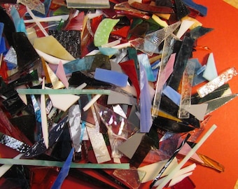 May include: A large pile of colorful glass pieces in various shapes and sizes. The glass pieces are arranged on a red surface.