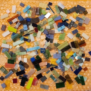 May include: A large collection of colorful glass mosaic tiles in various shapes and sizes. The tiles are arranged in a random pattern on a textured orange surface.