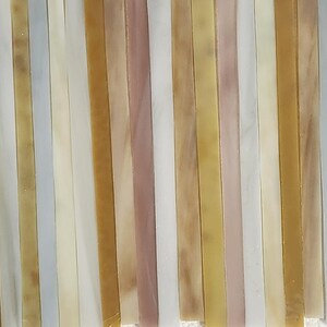 May include: A collection of thin, rectangular glass tiles in various shades of beige, brown, and white. The tiles are arranged in a vertical pattern, creating a striped effect.