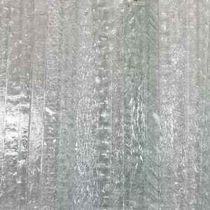 May include: A close-up of a silver metallic surface with a textured, striped pattern. The surface has a subtle sheen and appears to be made of metal.