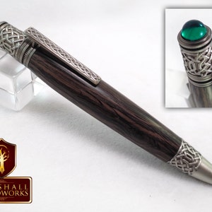 May include: A black and silver pen with a green gemstone top and Celtic knot design. The pen is made by Marshall Woodworks.