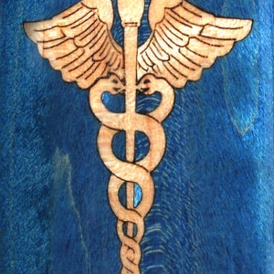 May include: A wood-burned image of the caduceus, a symbol of medicine, on a blue background.