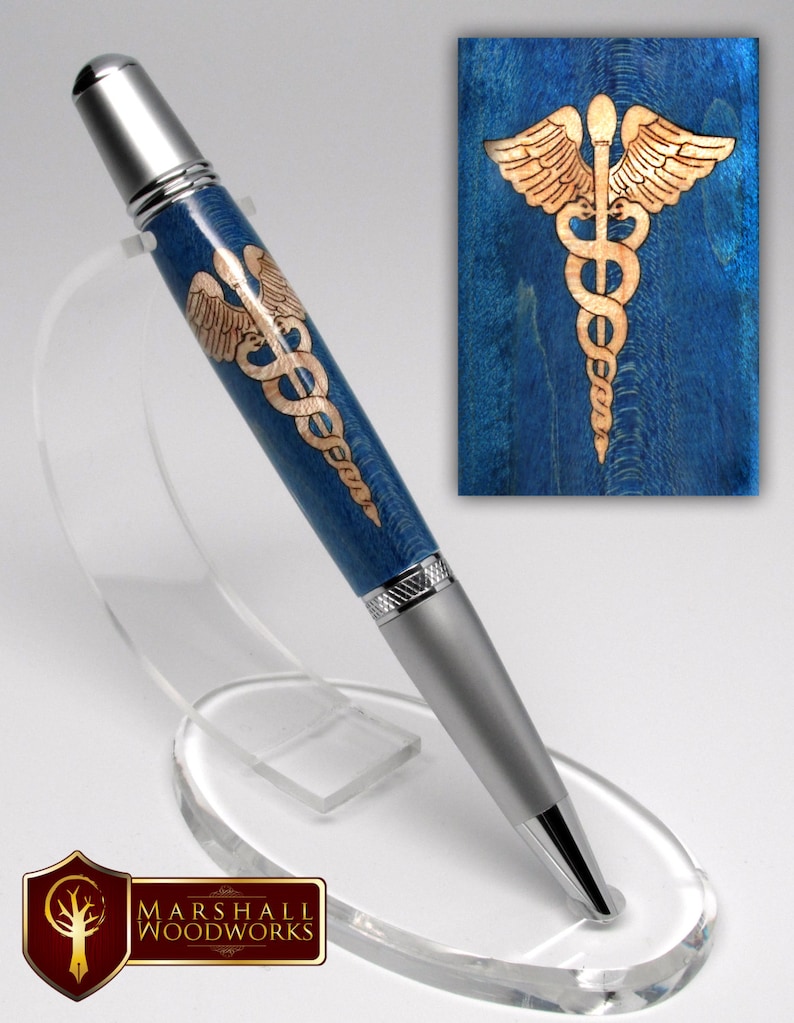 May include: A blue and silver pen with a medical caduceus design on the barrel. The pen is on a clear acrylic stand. The caduceus is a symbol of medicine and healing.