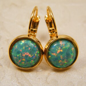 May include: A pair of gold hoop earrings with a round, green opal gemstone in each earring.