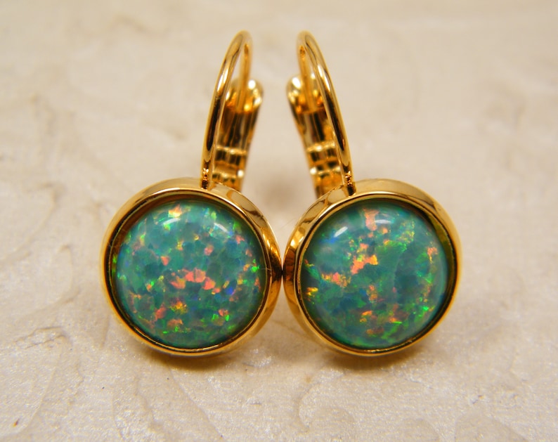 May include: A pair of gold hoop earrings with a round, green opal gemstone in each earring.
