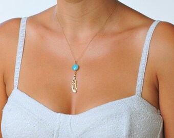 May include: A gold necklace with a turquoise pendant shaped like a feather. The necklace is worn by a person with a white tank top.