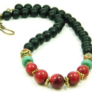 Puede incluir: Un collar de cuentas de &oacute;nix negro con cuentas de coral rojo y turquesa y detalles dorados.