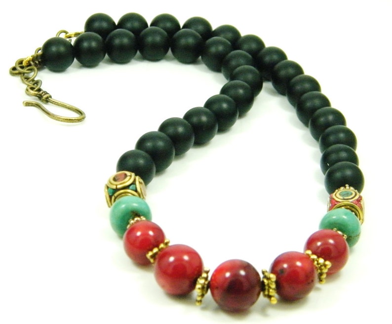 Puede incluir: Un collar de cuentas de &oacute;nix negro con cuentas de coral rojo y turquesa y detalles dorados.