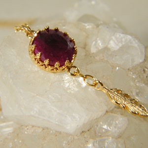 May include: A gold necklace with a ruby gemstone pendant and a gold feather charm.