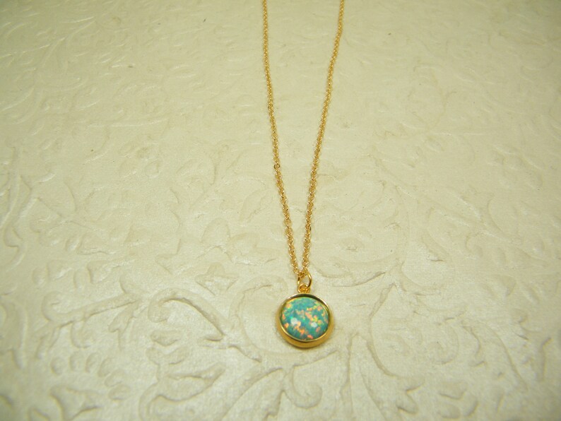 May include: A gold chain necklace with a round, light blue and white opal pendant.