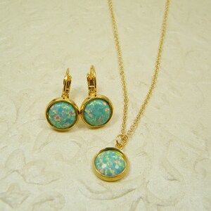 May include: A gold necklace and earrings set with a light blue opal stone pendant and matching earrings.