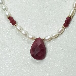 May include: A delicate necklace with a teardrop-shaped ruby pendant, surrounded by white pearls and small red beads.